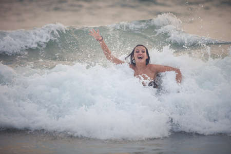 beautiful brunette young girl in brown bra drowning in the white sea wavesの写真素材
