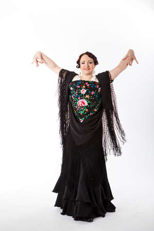 young beautiful brunette female spanish flamenco dancer in white shirt and black flamenco skirt posing with black flower shawl in her arms in studio on gray backgroundの写真素材