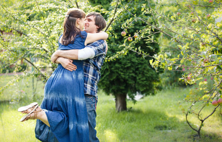 young handsome man in blue shirt kissing his beautiful brunette girl in blue dress in green garden