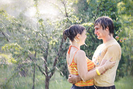 young handsome man with his beautiful brunette girlfriend stand under rain in green gardenの写真素材