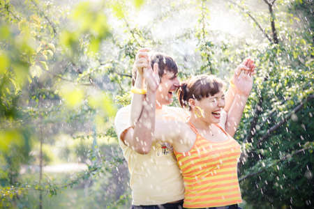 young handsome man with his beautiful brunette girlfriend stand under rain in green gardenの写真素材