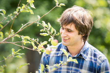 young handsome man in blue shirt sniffing flowers in green gardenの写真素材