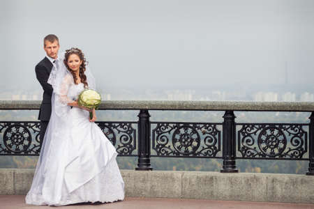 young handsome groom hold his beautiful brunette bride in white wedding dress on big city backgroundの写真素材