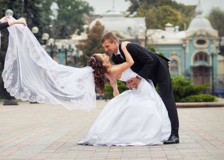 young handsome groom in black suit look at his beautiful brunette bride in white wedding dress on big city backgroundの写真素材