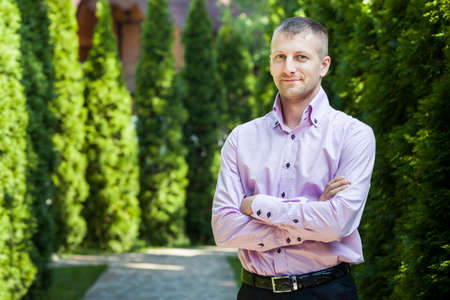 handsome man in pink shirt look at the camera with green trees on backgroundの写真素材