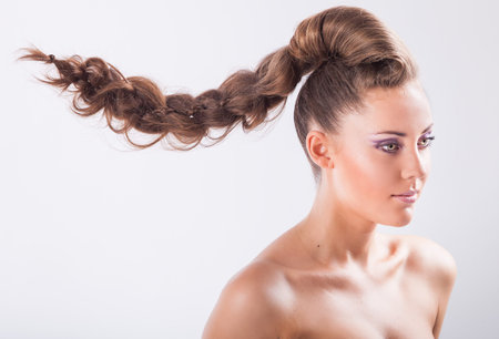 Portrait of beautiful young girl with stylish makeup and hair in studio on gray background