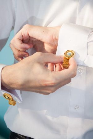 groom straightens cuffs on the sleeves of his white shirt