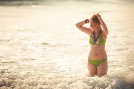 beautiful blonde girl in green swimming suit pose at sea wavesの写真素材