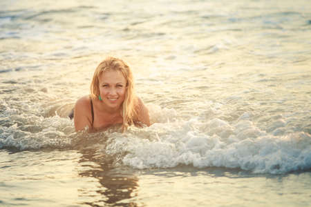 beautiful blonde girl in green swimming suit pose at sea wavesの写真素材