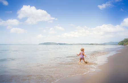 small blonde baby girl in purple swim suit play with waves on seashoreの写真素材
