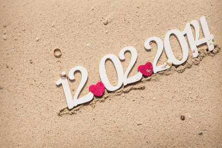 golden wedding rings lay on red hearts with date of marriage on background on white sandの写真素材