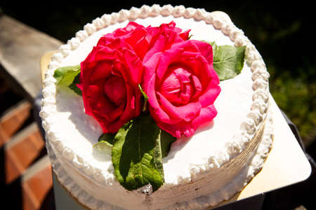 closeup beautiful white creamy delicious cake decorated with three red roses on the topの写真素材