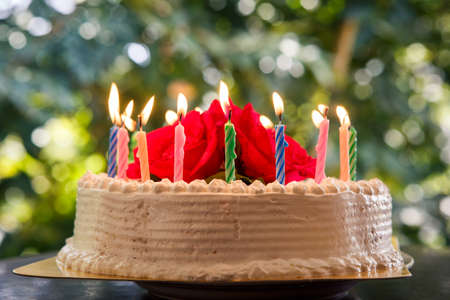 candle burning on a cream white creamy delicious cake decorated with three red roses on the  top closeupの写真素材