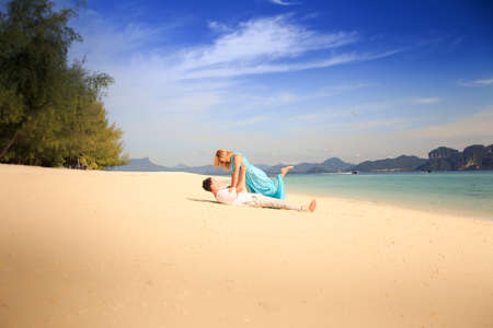 handsome man hold on his hands beautiful blonde woman in elegant dress with blue sea and mountains on backgroundの写真素材