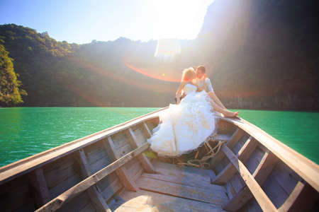 blonde bride and handsome groom sit on longtail boat in Thailandの写真素材