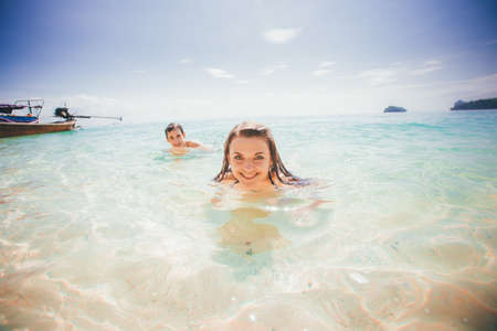 girl and guy swim in azure sea smiling against boat and islandの写真素材
