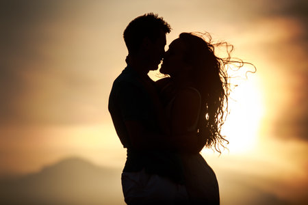 silhouette of kissing guy and girl against sun at dawn