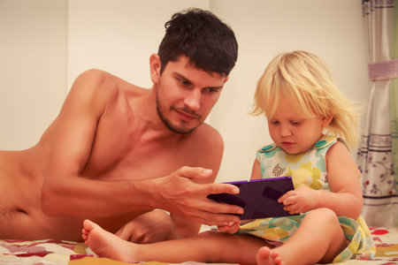 young father shows smartphone to his blonde two years old daughterの写真素材