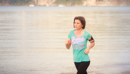 brunette girl in sports clothes runs on sand beach at low tide against sea at dawn