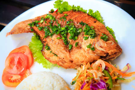 closeup view of fried fish with rice and vegetables on white big plate on tableの写真素材