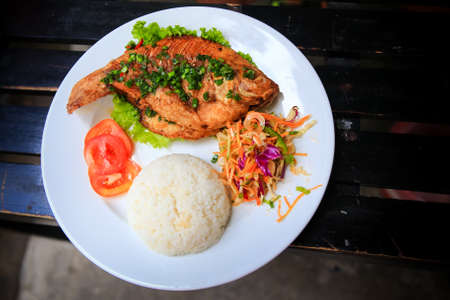 view of fried fish with rice and vegetables on white big plate on tableの写真素材