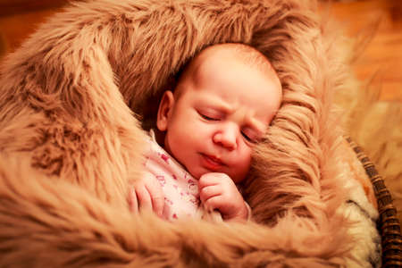 closeup portrait of newborn baby sleeping face with small hand near cheek covered with brown sheepsの写真素材