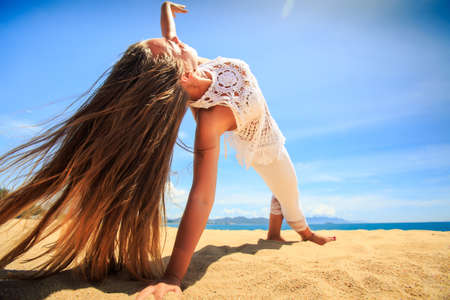 blonde girl girl in white lace costume closeup in yoga asana arm balance on beach against azure seaの写真素材