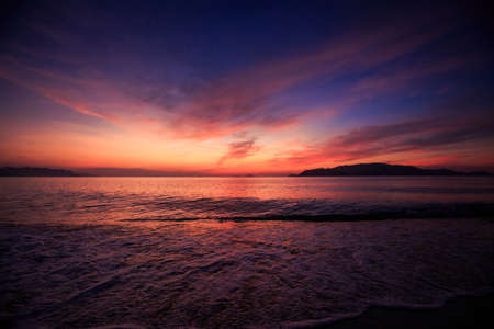 panorama of fantastic beautiful dark blue and red sky with fleecy clouds before sunrise and sea on foregroundの写真素材