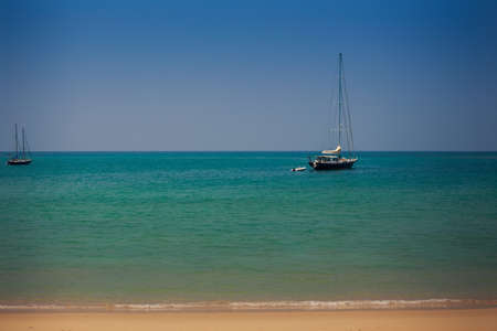 closeup two yachts in tranquil azure sea near sand beach against dark blue skyの写真素材