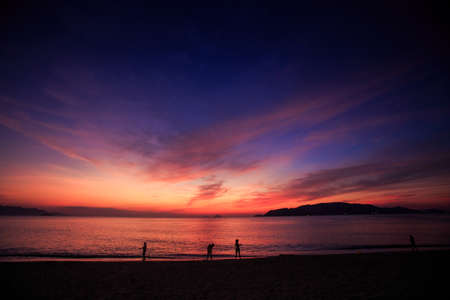 silhouettes of people on beach against sea and dark blue and red sky before sunriseの写真素材