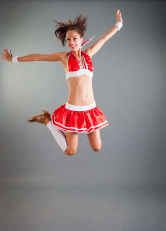 beautiful slim brunette girl in open red dance costume flies in dance position jumping in studio on grey backgroundの写真素材
