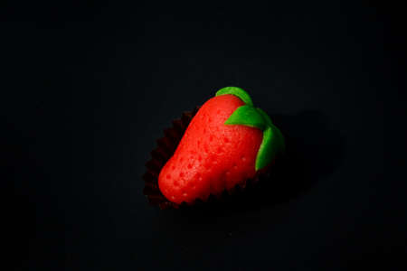 one red strawberry with green leaf shaped candy made from sugar marzipan on black backgroundの写真素材