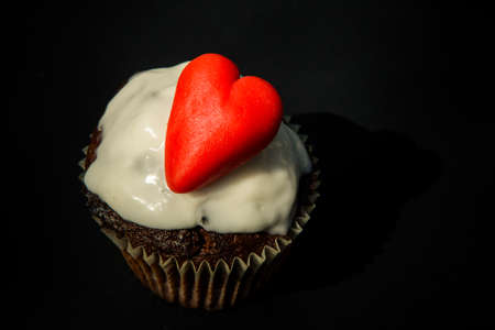 tasty homemade chocolate cupcake decorated with red heart shaped candy made from sugar marzipan on black backgroundの写真素材