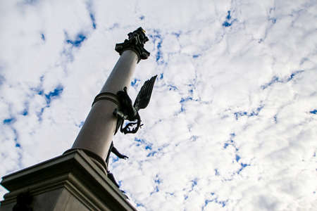 gorizontal inclined photo of column monument from downwards against blue sky and white cumulus clouds in old european cityの写真素材