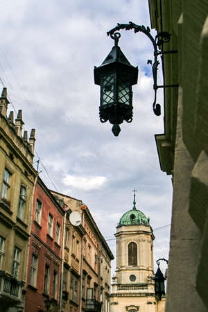 closeup age-old buildings iron lace streetlamp on stone wall at foreground and distant church in old european cityの写真素材