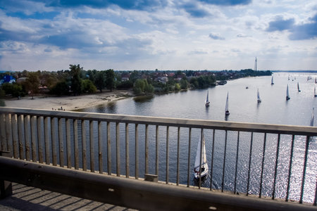 panorama from iron bridge of sailing  boats on wide river in city and bright sun reflection against...