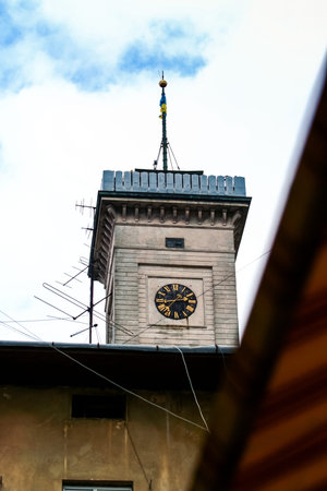 City Hall tower clock with bacon and private house antennas against sky from garret window
