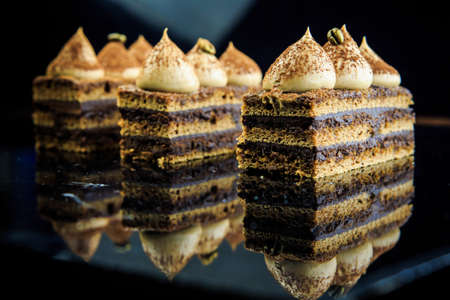 three chocolate opera cake slices decorated with white cream on black mirror backgroundの写真素材