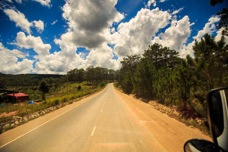 sunny highway vanishes into space among hilly country land against cloudy blue skyの写真素材