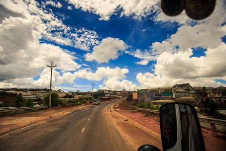 Distant green-houses behind brown ground field and road in Vietnamese country land against cloudy blue skyの写真素材