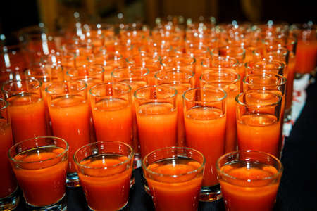 set of glasses with orange juice arranged in rows on black table on catering service banquetの写真素材