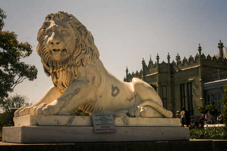 side view of age-old white marble lion sculpture in park against Vorontsov palace and blue sky in Crimeaのeditorial素材