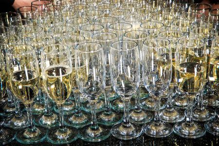 set of partially filled champagne glasses arranged in triangle on mirror background on catering...
