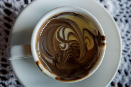 top view of white cup of hot mixed black, milk and white chocolate served on white knitted napkin backgroundの写真素材