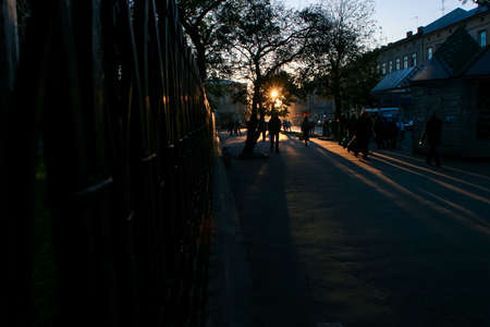 people silhouettes on dark old city street at back-light of sun through trees at sunset in european city Lvovの写真素材
