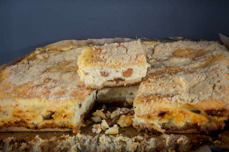 one small piece of handmade  cheesecake with raisins stands on whole pie served on wooden tablet against gray backgroundの写真素材