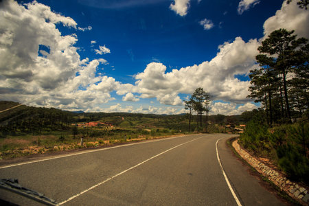 sunny highway bend against hilly wooded country land and blue cloudy sky