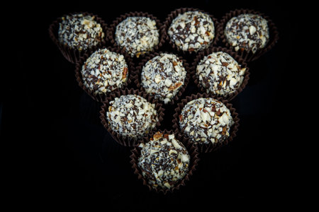 nine round big chocolate candies with coconut shavings served on black mirror background with...