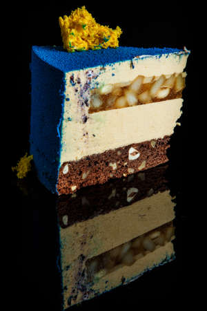 vertical view of piece of delicious blue mousse cake with yellow sponge cake decoration on top and caramel pear inter-layer stands on black mirror backgroundの写真素材