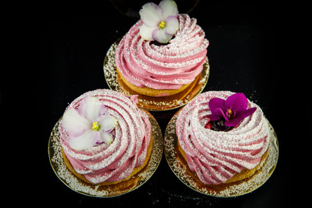 top view on three pink zephyr cookies decorated with violet and white flowers on black mirror...